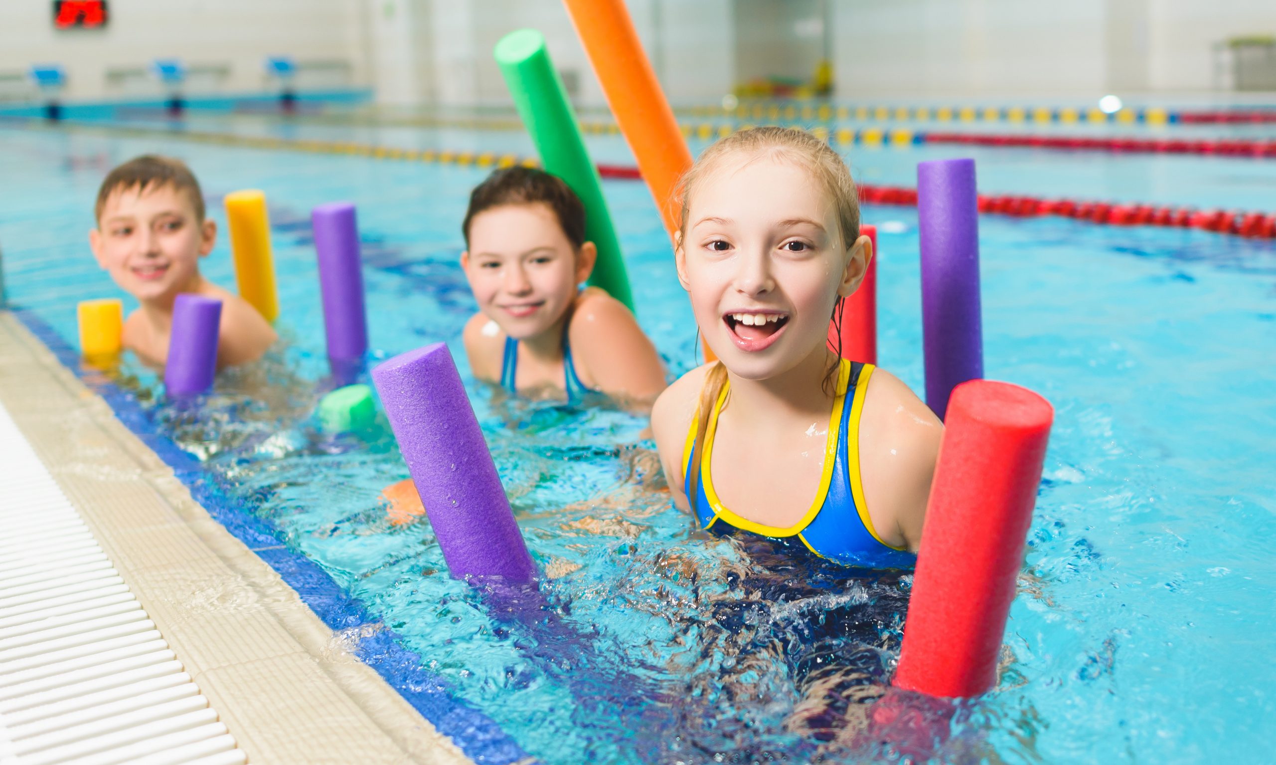 Happy and smiling group of children learning to swim with pool noodle.